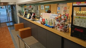 Un espace d’accueil d’hôtel comprenant un comptoir, divers équipements et un réfrigérateur contenant des boissons Coca-Cola.