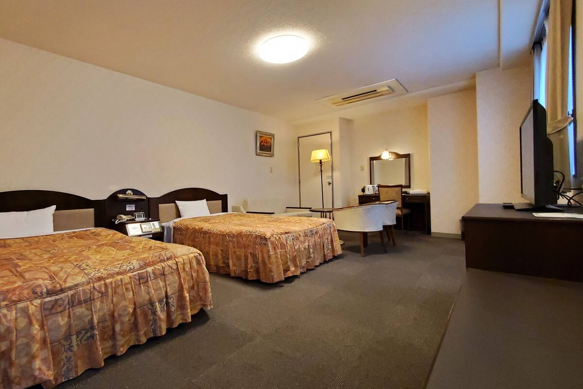 Une chambre d’hôtel avec deux lits, un bureau, une chaise, une lampe de bureau, un miroir et un téléviseur.