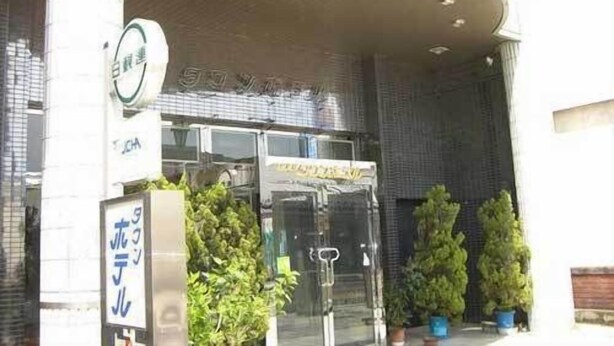 Entrada de hotel con puerta de vidrio, un cartel y plantas en macetas.