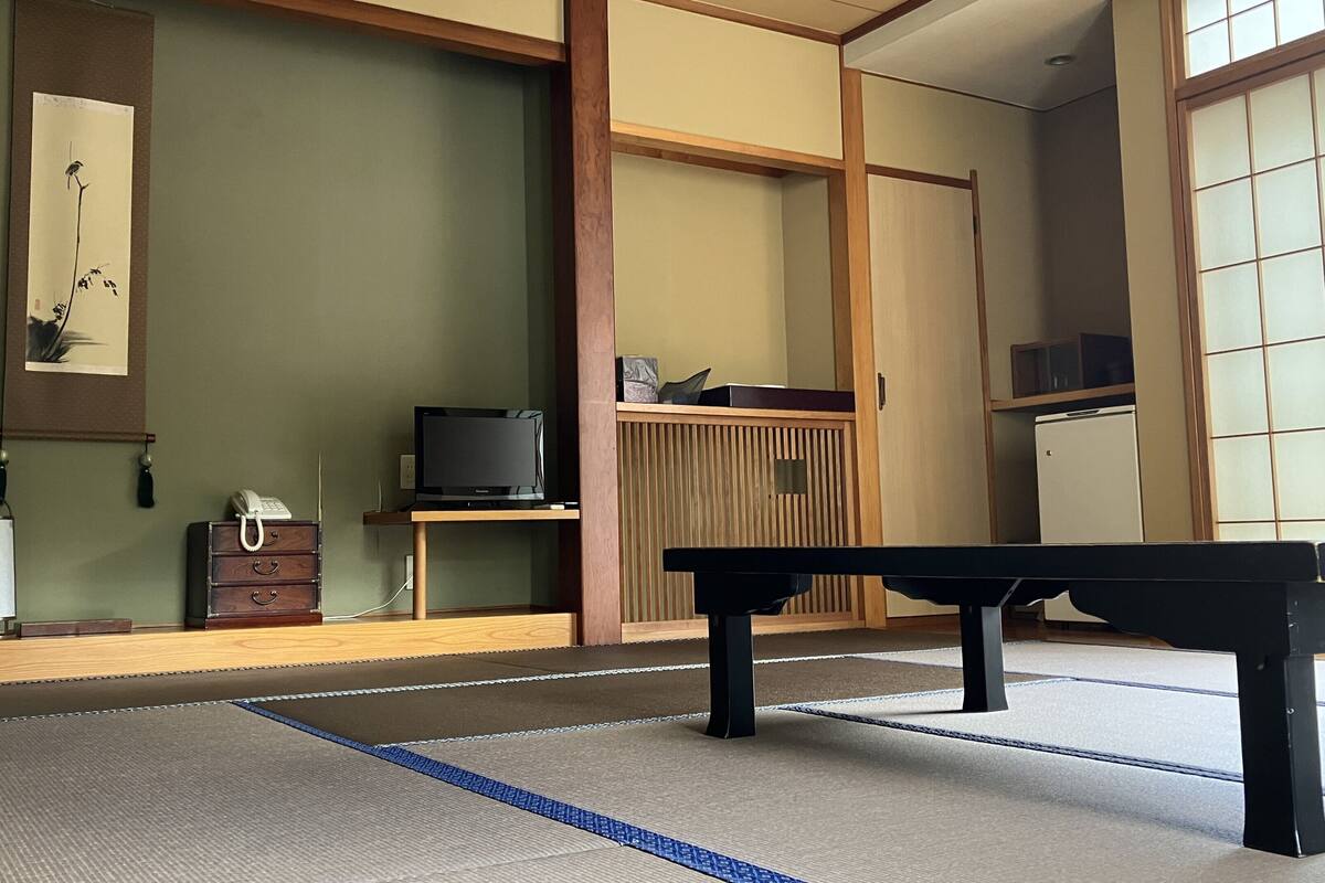 Ein Raum mit Tatami-Matten, einem Fernseher, einem Telefon und einem traditionellen japanischen Schrank.