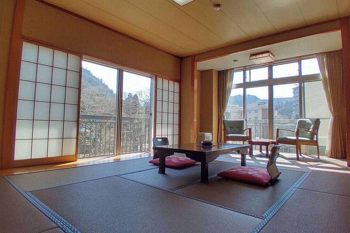 Ein Raum mit Tatami-Matten, Schiebetüren, einem niedrigen Tisch und Stühlen.