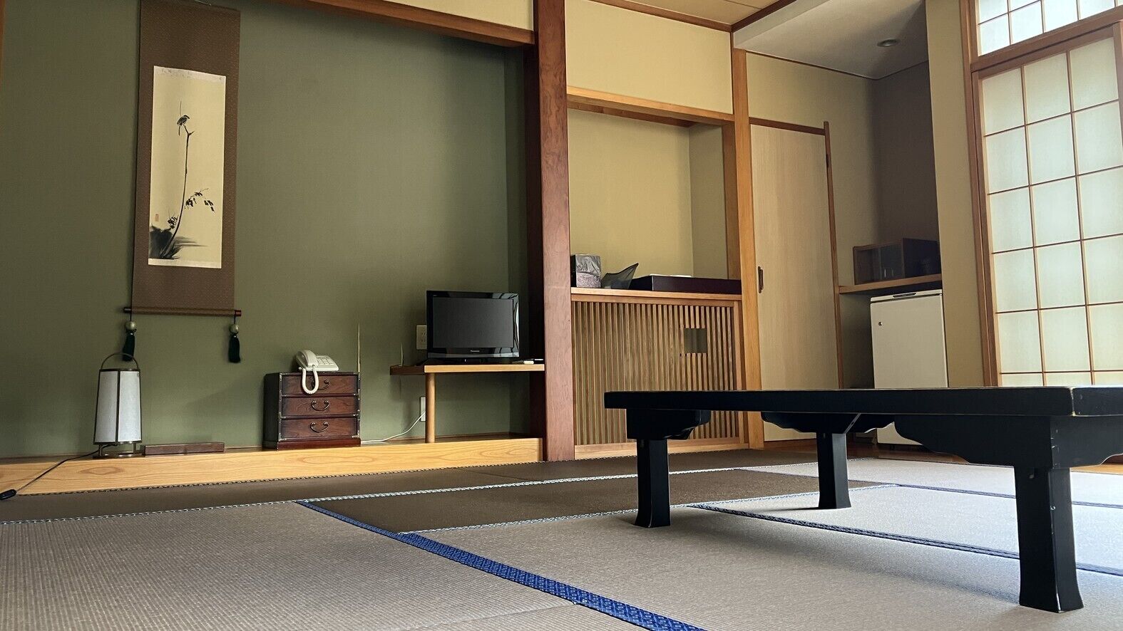 Una habitación con tatami, una mesa baja, un televisor sobre un soporte de madera y una puerta corredera.