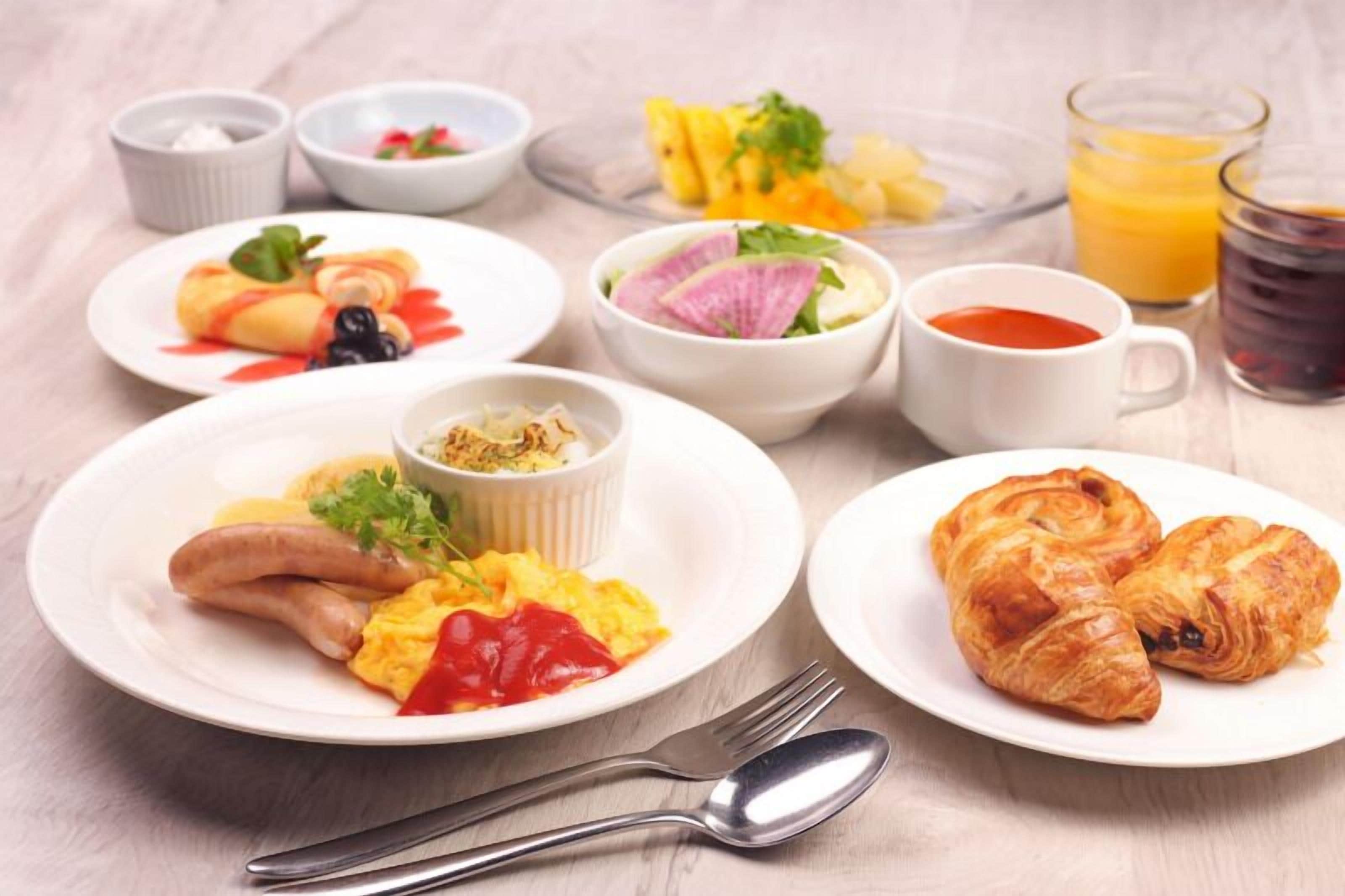 Una mesa de desayuno con platos de comida, un vaso de jugo de naranja y una taza de café.