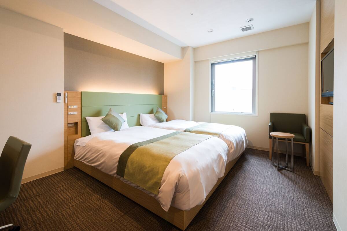 A hotel room with a large bed, a small desk, a chair, and a window.
