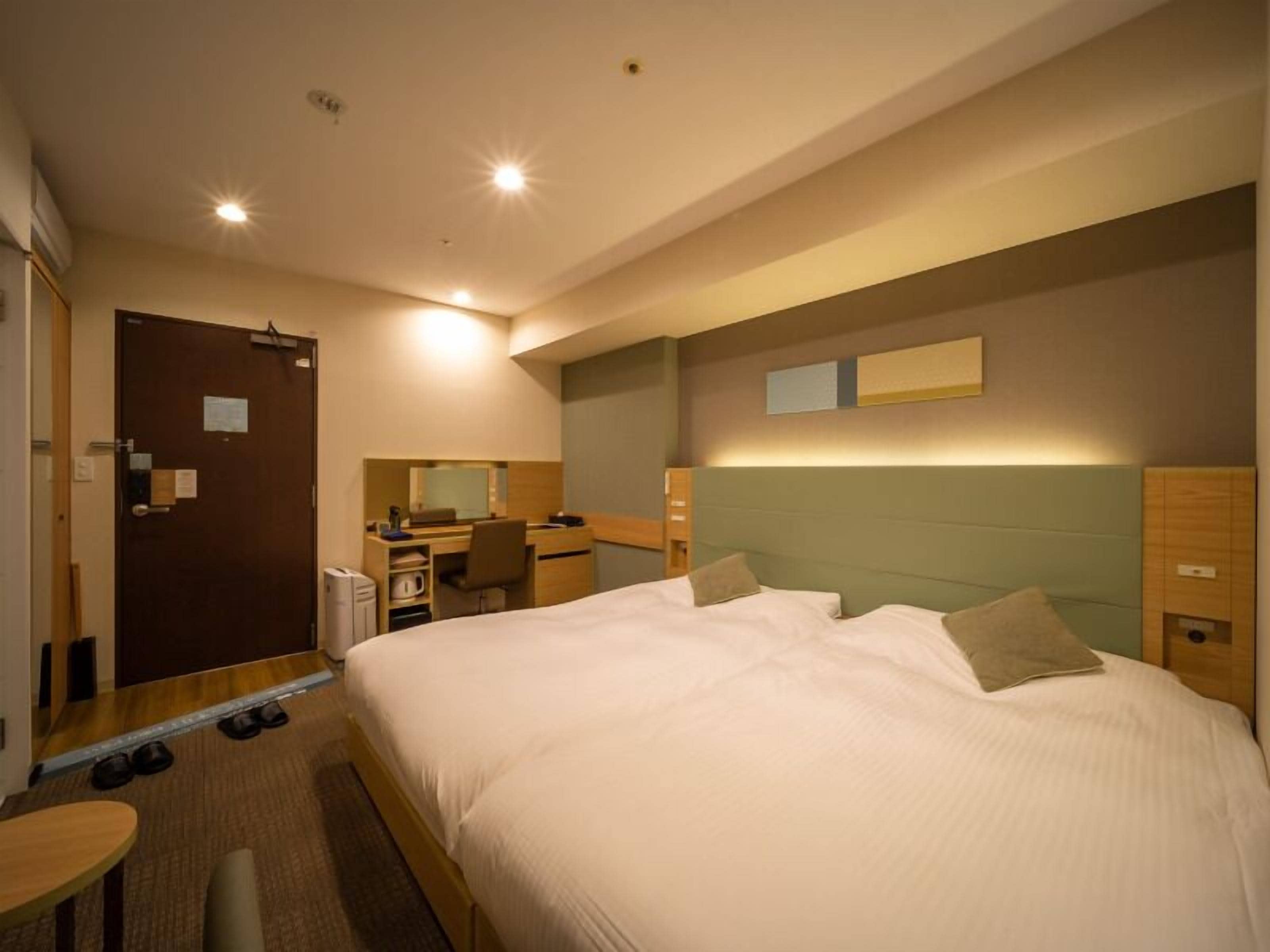 A hotel room with a bed, desk, chair, and a small table.