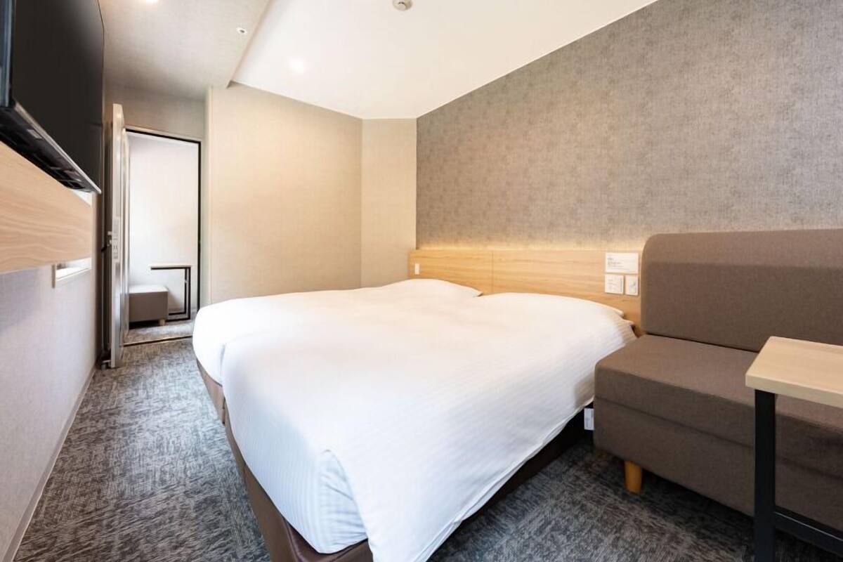 A hotel room with a bed, a sofa, a small table, and a TV mounted on the wall.