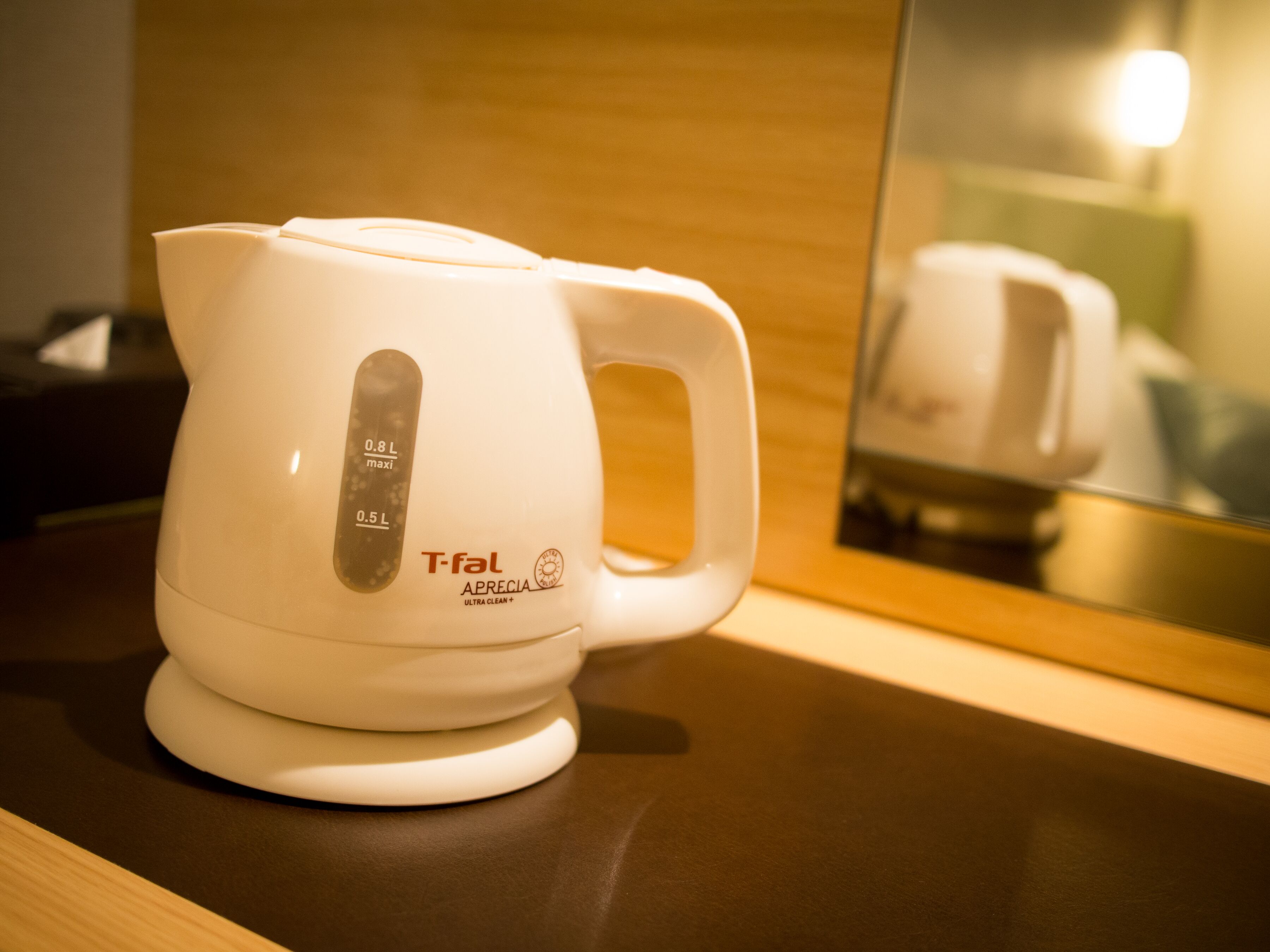 A white T-fal coffee maker with a handle and a digital display on a dark countertop.