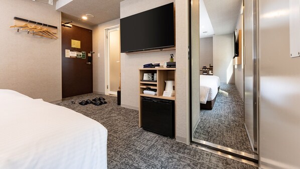 Habitación de hotel con cama, televisor montado en la pared, minibar y un espejo que refleja la habitación.