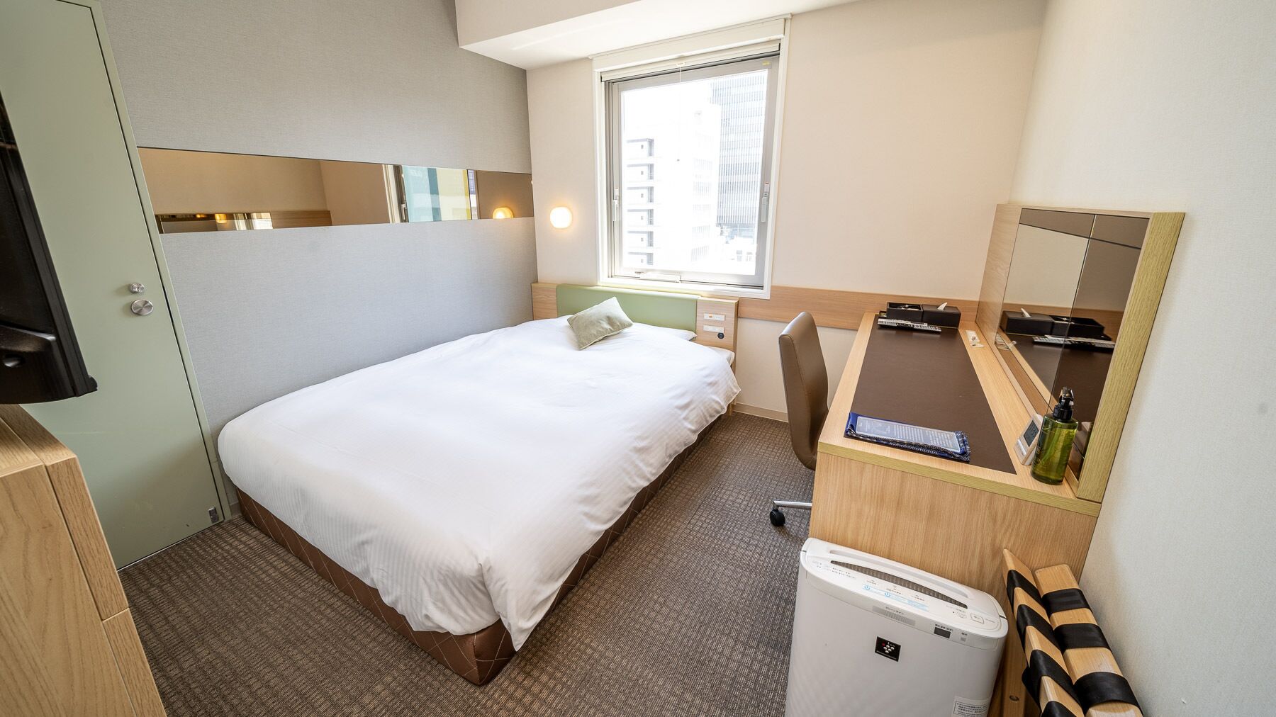 Een hotelkamer met een bed, een bureau, een spiegel, een raam en een kleine airconditioning.