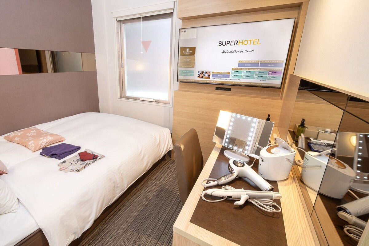 A hotel room with a bed, a desk with a mirror, and a TV displaying 'SuperHotel' branding.