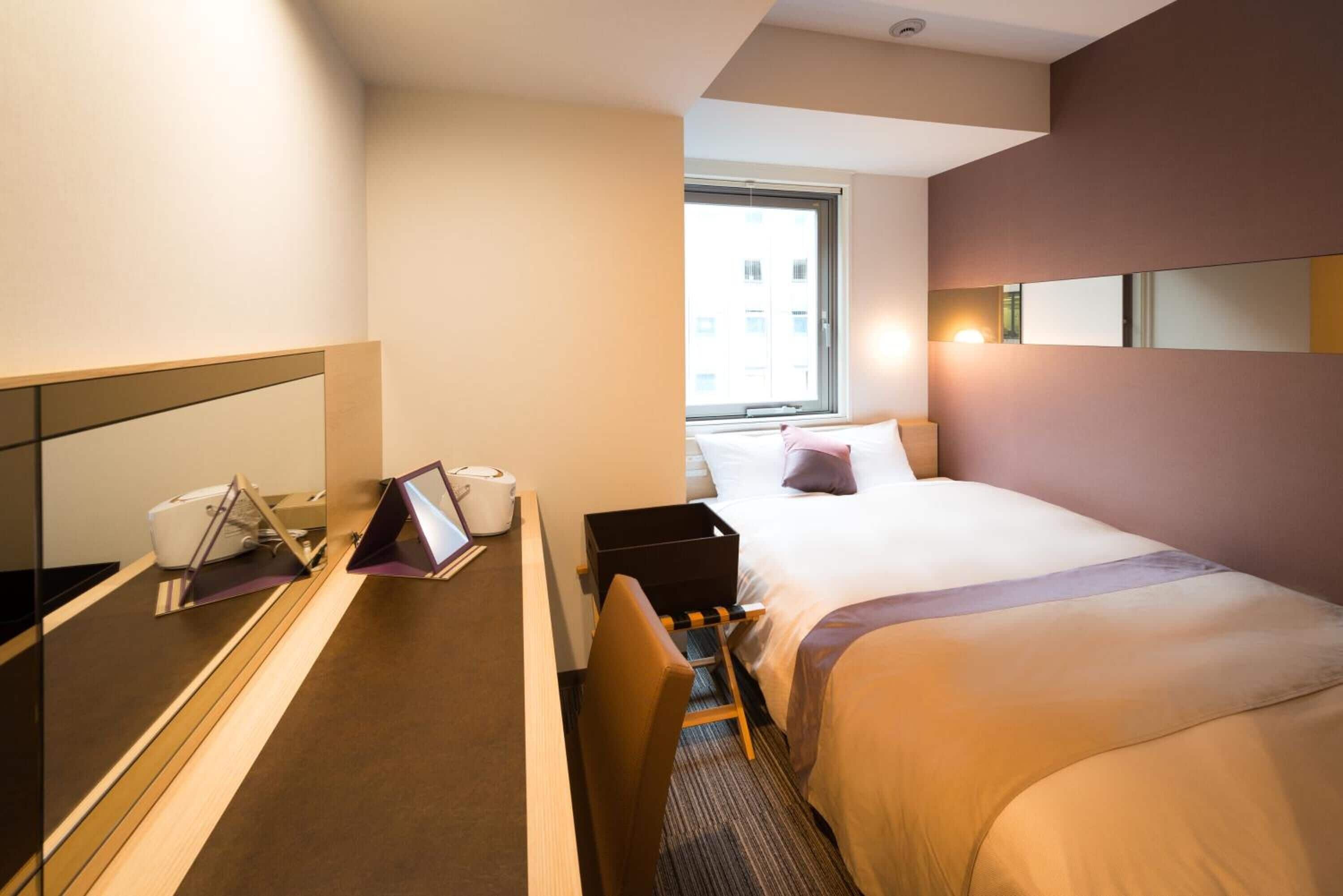Une chambre d’hôtel avec un lit, une table de chevet, une chaise et un grand miroir.