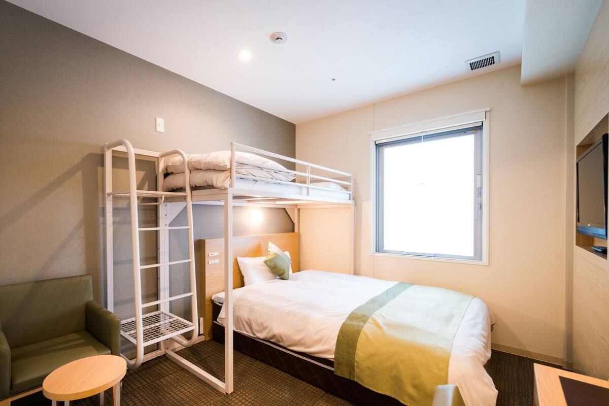 A bunk bed room with a desk, a chair, and a window.