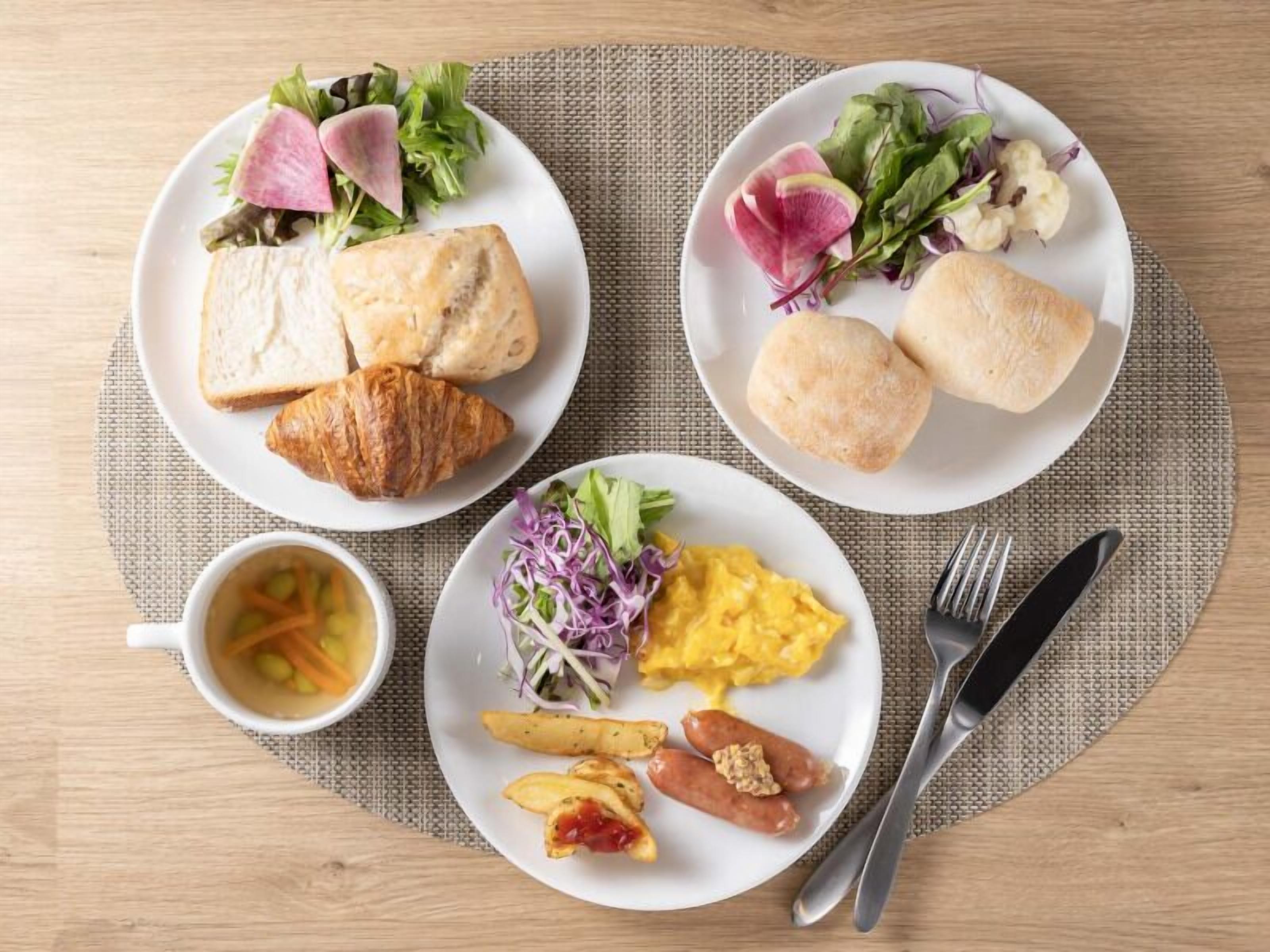 Three plates of food with bread, salad, and a cup of soup.