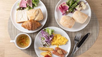 Three plates of food with bread, salad, and a cup of soup.