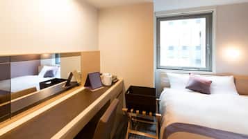 A hotel room with a bed, a desk with a laptop, a chair, a small table, a mirror, and a window.