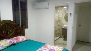 Une chambre à coucher avec un lit, une fenêtre et une salle de bain visible à travers une porte ouverte.
