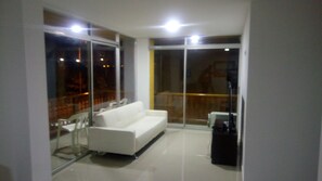Een moderne woonkamer met een witte bank, een glazen deur naar een balkon en een kleine tafel.