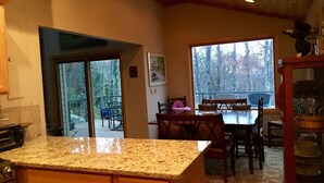 Eine Küche mit Granit-Arbeitsplatten, Holzschränken und einem Essbereich mit Blick auf Bäume durch große Fenster.