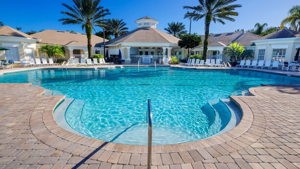 Ein großer, klarer Pool mit Liegestühlen und Palmen, umgeben von einer Pflasterterrasse.