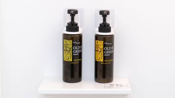Two bottles of olive green hair and body shampoo on a white shelf.
