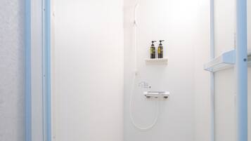 A small, white shower room with a white door, a white showerhead, and two bottles of shampoo on a shelf.