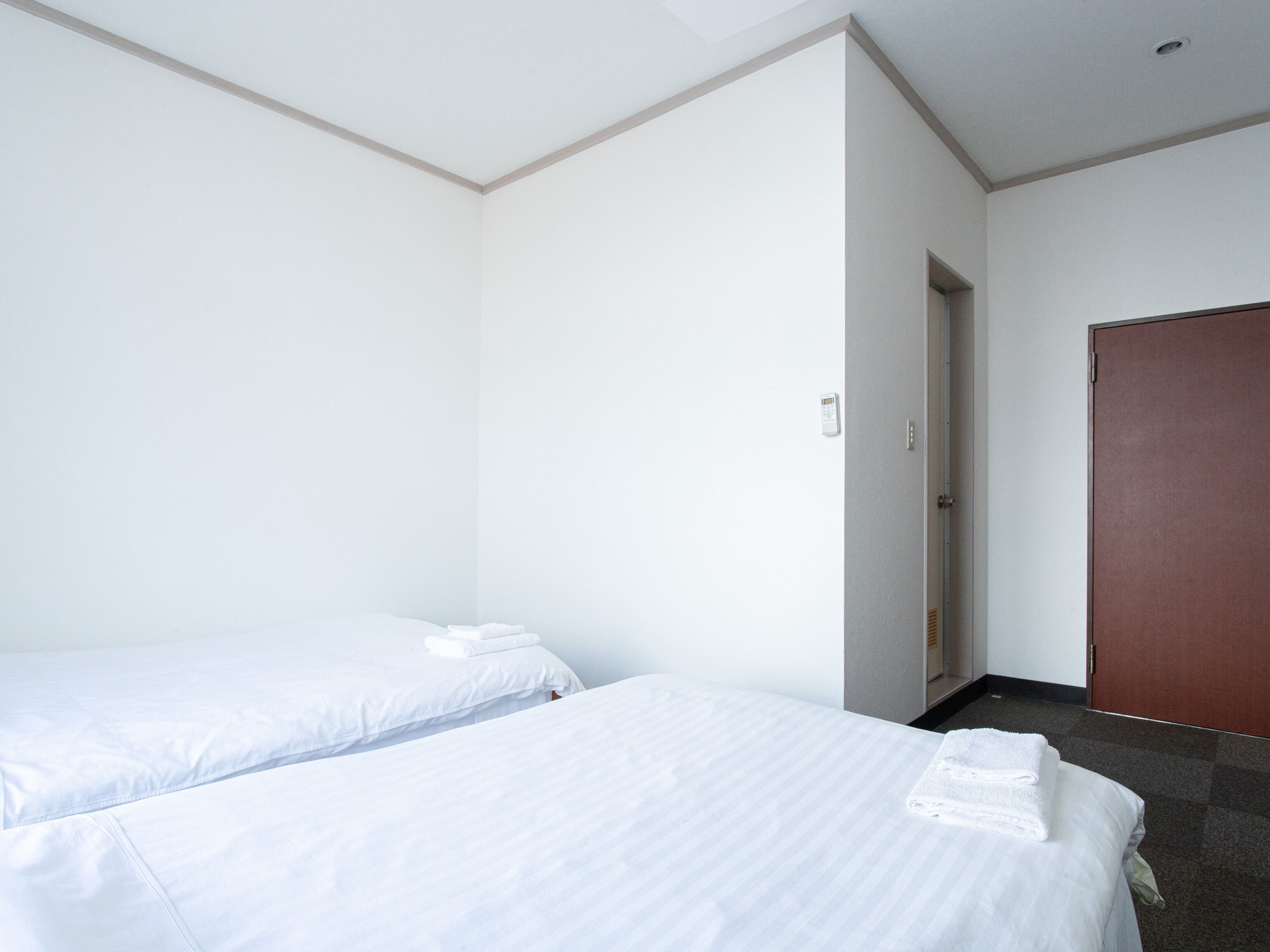 Habitació d'hotel amb dos llits individuals, una porta de fusta i un bany petit visible per una porta oberta.