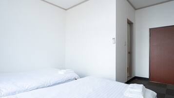 Habitació d'hotel amb dos llits individuals, una porta de fusta i un bany petit visible per una porta oberta.