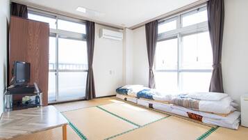 Habitación de hotel con una cama, un televisor en un mueble bajo, una mesita y una ventana con cortinas.