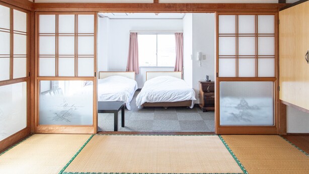 Una habitación japonesa tradicional con suelo de tatami, dos camas, puertas correderas y vistas a un dormitorio con ventana.