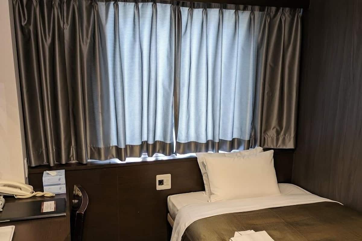 Una habitación de hotel con cama, escritorio, teléfono y ventana con cortinas.