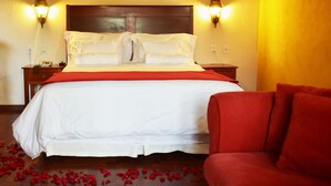 A hotel room with a large bed, two bedside lamps, a red sofa, and a painting on the wall.