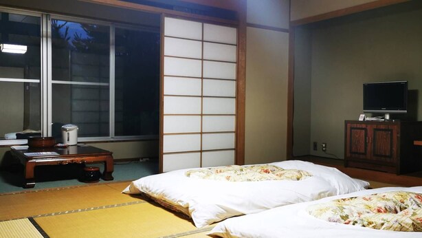 A traditional Japanese room with tatami flooring, two beds with floral bedding, a television on a cabinet, and a sliding shoji screen. - Shiozawa Onsen Shichihokan (Takayama)