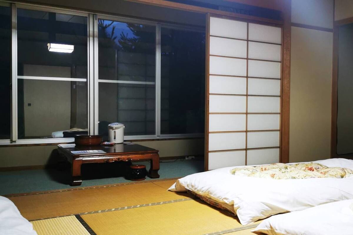 Habitació japonesa tradicional amb tatami, dos llits amb roba de llit floral, una televisió sobre un moble i un panell shoji corredís.