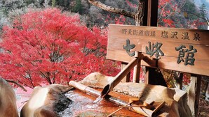 A traditional Japanese onsen with a wooden sign, a stone basin, and a backdrop of red foliage. - Shiozawa Onsen Shichihokan (Takayama)