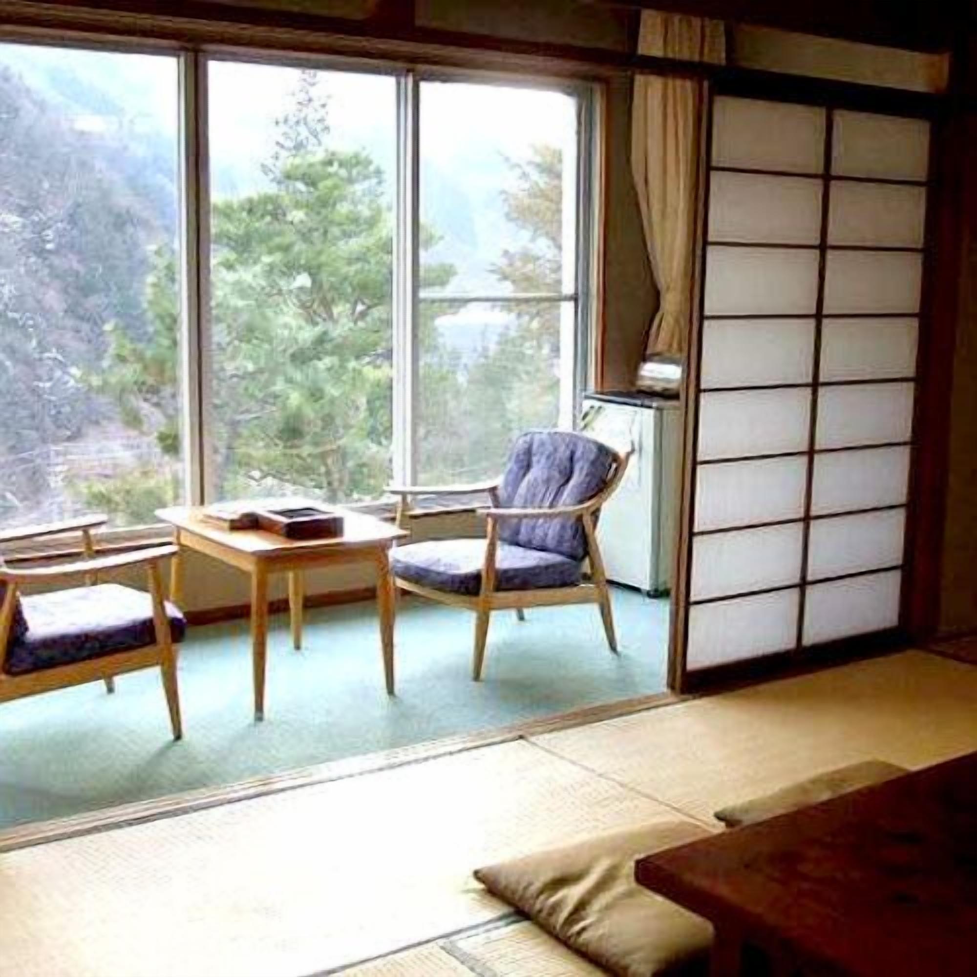 Una habitación con suelo de tatami, una mesa baja, una silla y un futón.