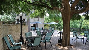 An outdoor patio with tables and chairs, surrounded by trees and a stone wall. - Blue River Condo on the Comal River (New Braunfels)