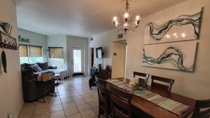 A spacious living area with a dining table, chairs, and a chandelier. There is a sofa and a coffee table in the background. - Blue River Condo on the Comal River (New Braunfels)