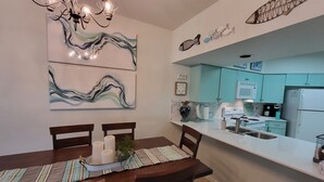 A modern kitchen with teal cabinets, a white countertop, and a dining area with a striped placemat and candles. - Blue River Condo on the Comal River (New Braunfels)