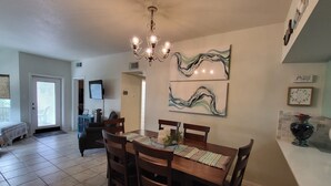A dining area with a wooden table, four chairs, a chandelier, and abstract wall art. - Blue River Condo on the Comal River (New Braunfels)