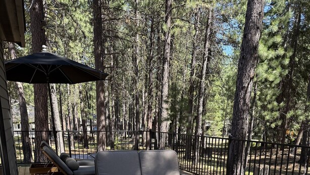 An outdoor deck with wicker furniture, a fire pit, and a view of a forested area. - NEXT TO GLAZE MEADOW, CUTE, WITH MANY AMENITIES! (Sisters)