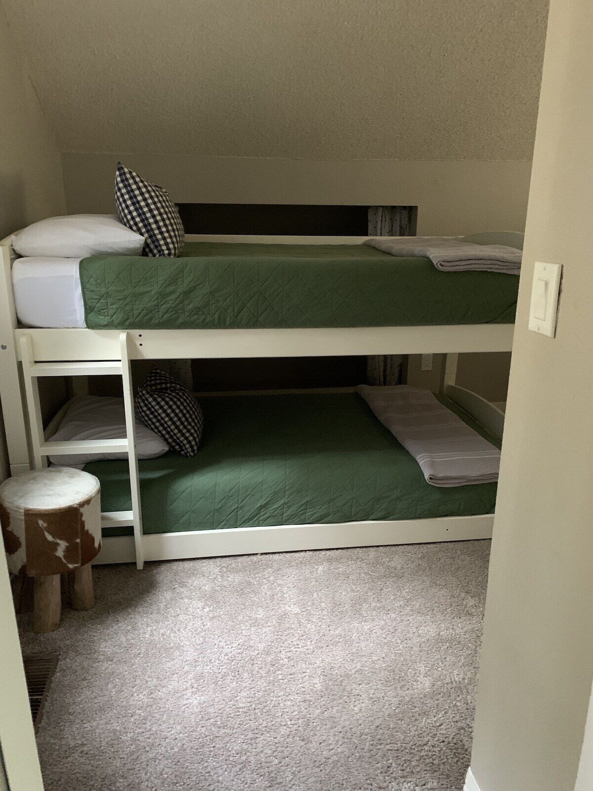 Une chambre avec un lit superposé, un matelas vert, du linge de lit blanc et un petit tabouret rond.