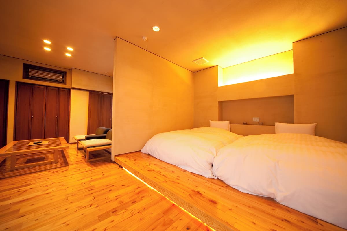 A room with a wooden floor, a bed with white bedding, a small table, and a chair.