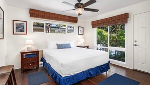 A bedroom with a large bed, two bedside lamps, a ceiling fan, and a view of the outdoors through a sliding glass door. - 🏖️Oceanfront Kona Condo | Top Floor + Sunset Views (Kailua Kona)