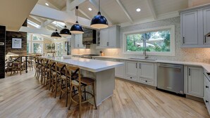 A spacious kitchen with a large island, bar stools, and a view of greenery through a window. - 12 Royal Tern - 2nd Row (70 yard walk) to the Ocean and Large Private Pool (Hilton Head Island)