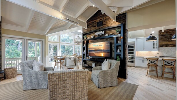 A spacious living area with a large TV, wicker furniture, and a view of the outdoors through large windows. - 12 Royal Tern - 2nd Row (70 yard walk) to the Ocean and Large Private Pool (Hilton Head Island)
