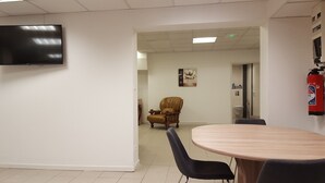 A conference room with a round table, two chairs, a television on the wall, a fire extinguisher, and a door leading to a bathroom.
