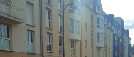 Una hilera de edificios residenciales de varios pisos con balcones, una farola y coches aparcados.