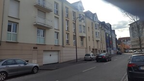A row of multi-story residential buildings with balconies, parked cars, and a clear sky.