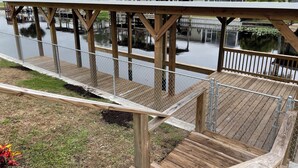Eine Holzterrasse mit Metallgeländer, die auf ruhiges Gewässer blickt, umgeben von Wohnhäusern und Grünflächen.