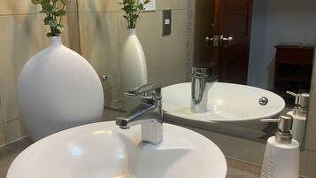 A bathroom with a round white sink, a mirror, and two white vases with plants.